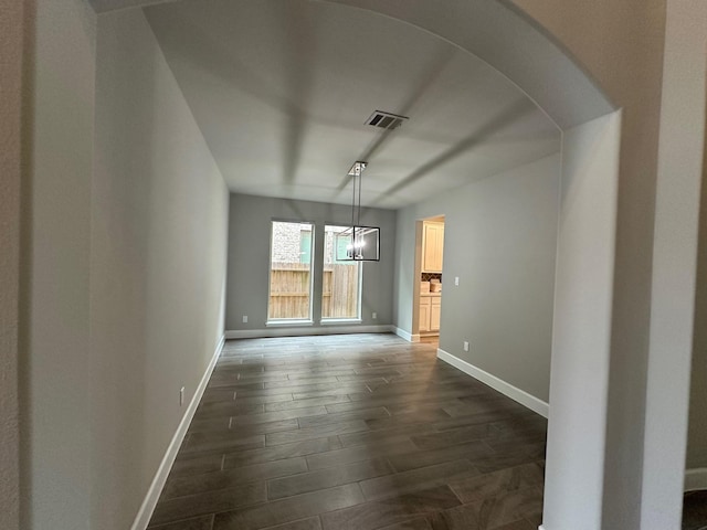 unfurnished dining area featuring visible vents, baseboards, arched walkways, and dark wood finished floors