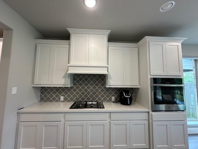 kitchen with stainless steel oven, light countertops, white cabinets, gas stovetop, and decorative backsplash
