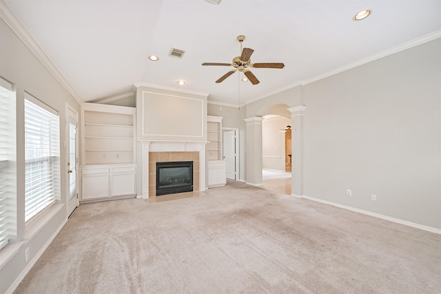 unfurnished living room with a tiled fireplace, visible vents, ornate columns, light colored carpet, and ceiling fan