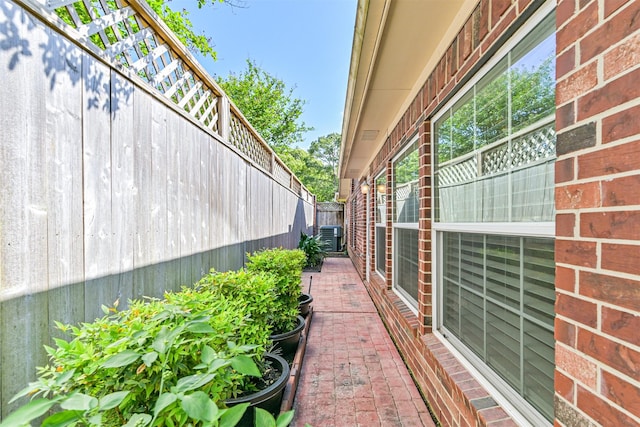 view of side of property featuring brick siding, central AC, and fence