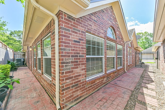 view of side of property with brick siding, fence, a patio area, and central AC