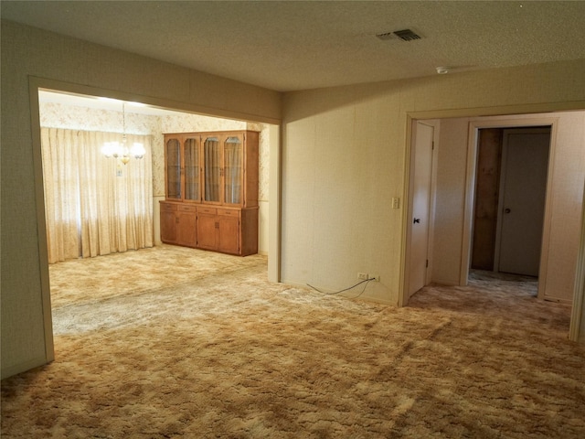 carpeted spare room featuring a textured ceiling, an inviting chandelier, and visible vents