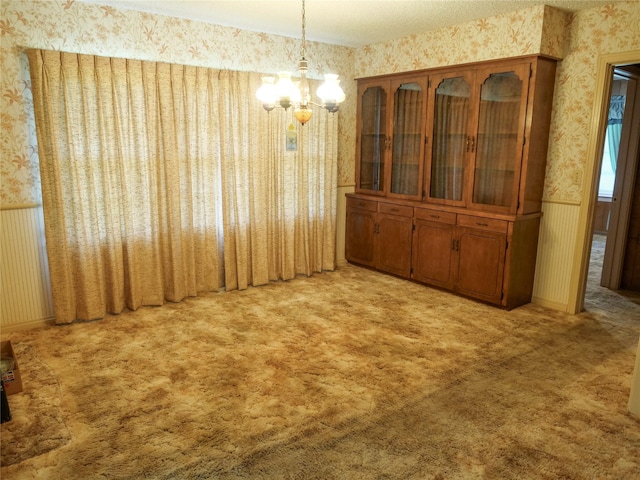 unfurnished dining area with wallpapered walls, an inviting chandelier, carpet, and a wainscoted wall