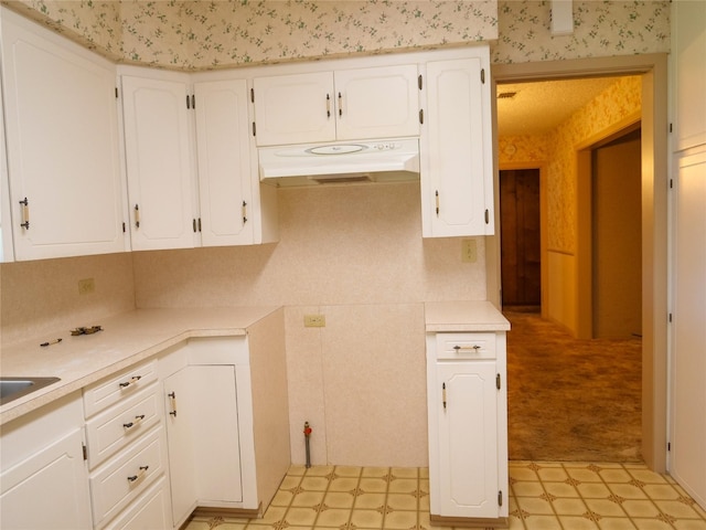 kitchen featuring light floors, white cabinetry, under cabinet range hood, light countertops, and wallpapered walls
