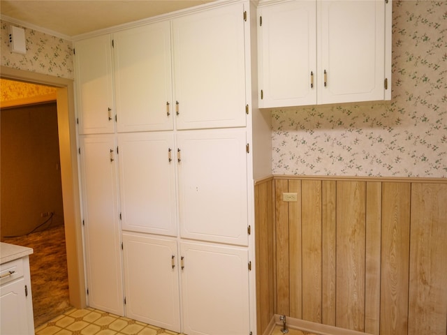 interior space with wallpapered walls, wooden walls, light countertops, a wainscoted wall, and white cabinets