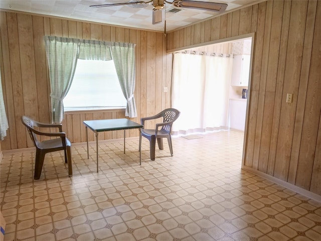 sitting room featuring wooden walls, ceiling fan, and light floors
