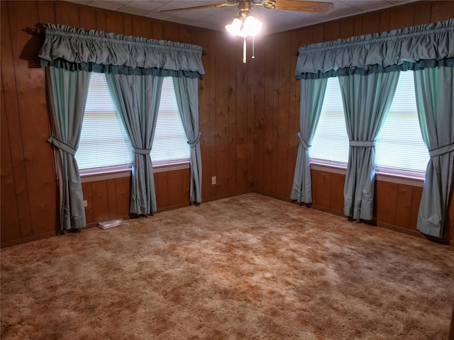 carpeted empty room featuring wood walls and a ceiling fan