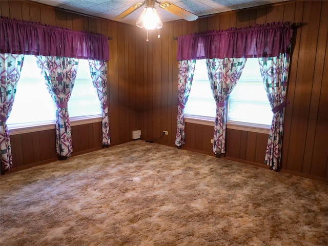 carpeted spare room with wood walls, ceiling fan, and a healthy amount of sunlight