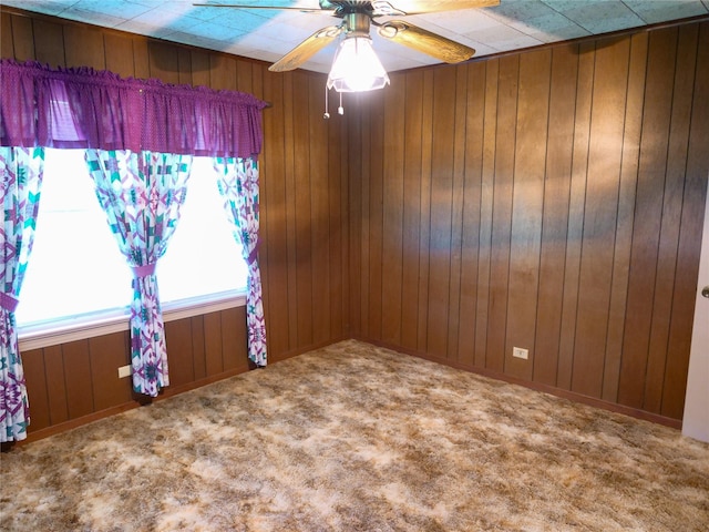 carpeted empty room featuring wood walls and ceiling fan