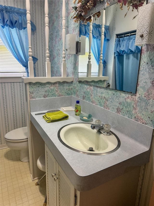 bathroom featuring plenty of natural light, vanity, wallpapered walls, and toilet
