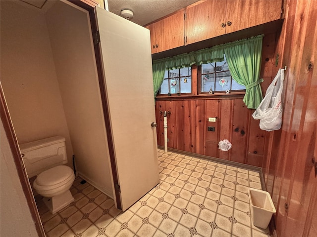 bathroom featuring toilet, tile patterned floors, wood walls, and a textured ceiling
