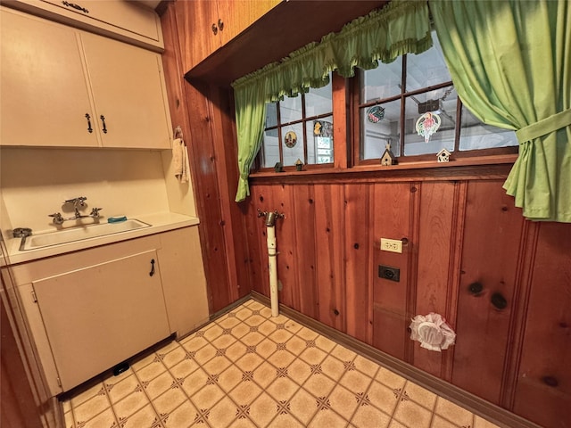 interior space featuring a sink, wood walls, cabinet space, and light floors