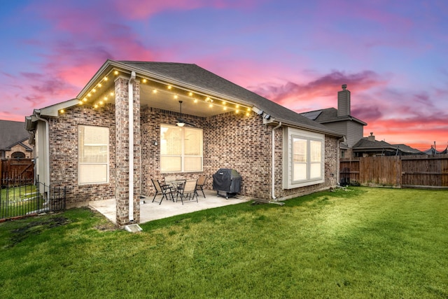 back of house at dusk with a yard, a chimney, a fenced backyard, a patio, and brick siding