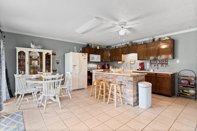 kitchen featuring a kitchen breakfast bar, white appliances, light tile patterned floors, a ceiling fan, and crown molding