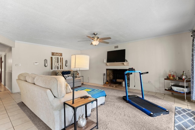 tiled living area with a fireplace with raised hearth, a textured ceiling, a ceiling fan, and crown molding