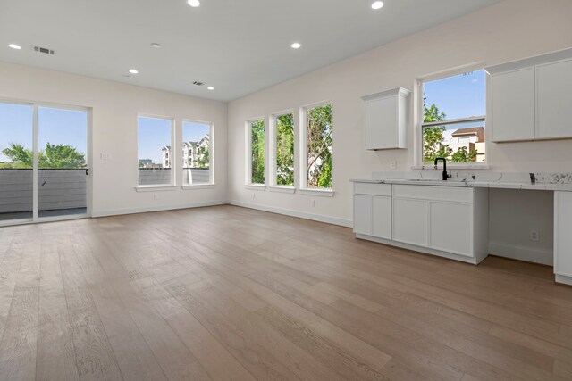 unfurnished living room with recessed lighting, plenty of natural light, light wood-style flooring, and a sink