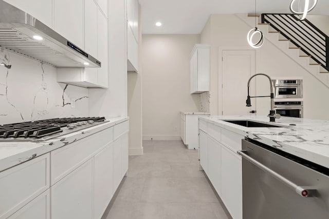kitchen with under cabinet range hood, light stone counters, appliances with stainless steel finishes, and a sink
