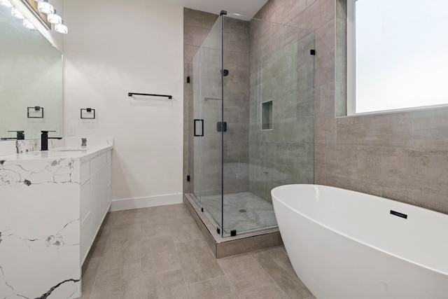 bathroom with a shower stall, vanity, a freestanding tub, tile patterned floors, and baseboards
