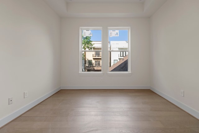 unfurnished room with a raised ceiling, light wood finished floors, and baseboards