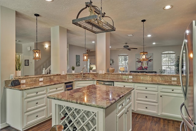 kitchen with a peninsula, a center island, a textured ceiling, stainless steel appliances, and a sink