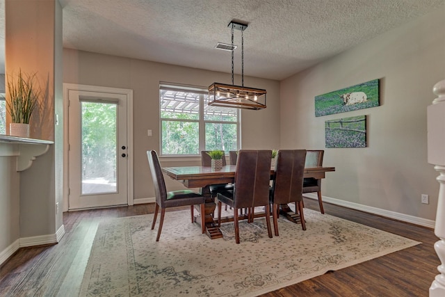 dining room featuring dark wood-style flooring, baseboards, an inviting chandelier, a textured ceiling, and visible vents