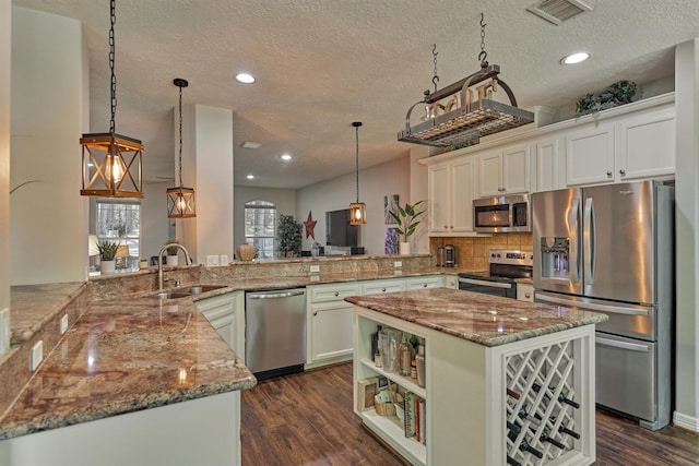 kitchen featuring visible vents, a peninsula, a textured ceiling, light stone countertops, and stainless steel appliances