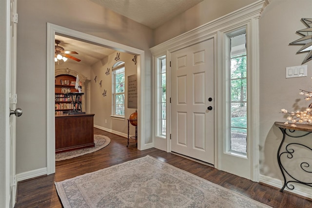foyer featuring a ceiling fan, baseboards, and dark wood-style floors