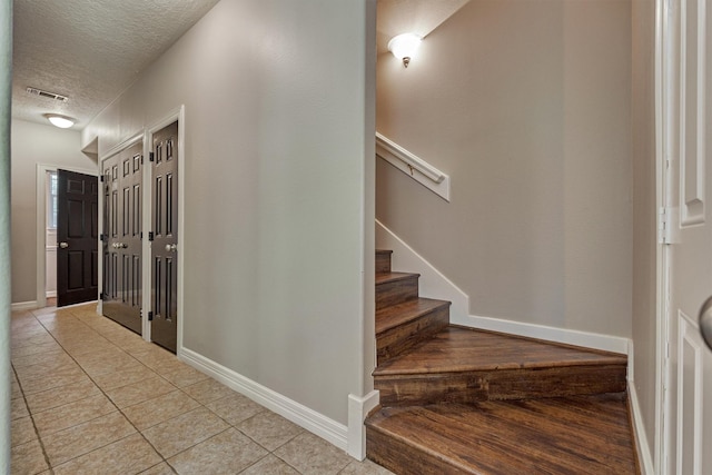 stairs with a textured ceiling, baseboards, tile patterned flooring, and visible vents