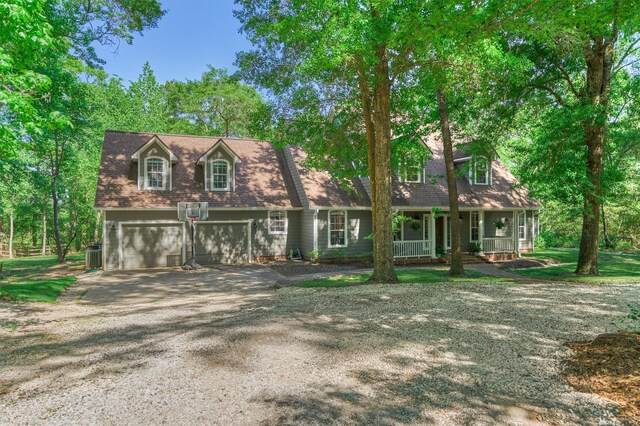 new england style home with a porch, driveway, a garage, and central AC unit
