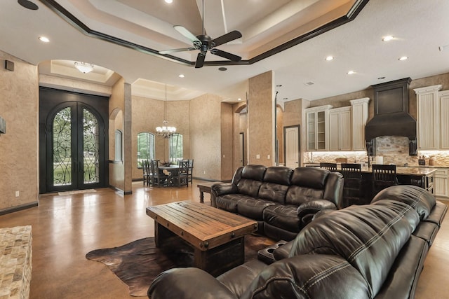 living room with arched walkways, ceiling fan with notable chandelier, a raised ceiling, concrete flooring, and french doors