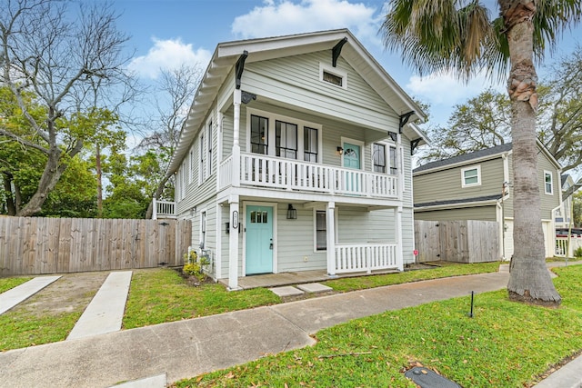 view of front facade with a balcony, a front yard, a porch, and fence