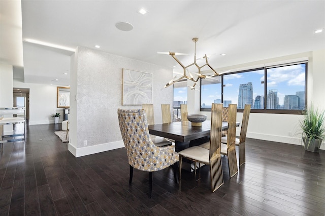 dining room featuring wood finished floors, a view of city, a notable chandelier, and baseboards