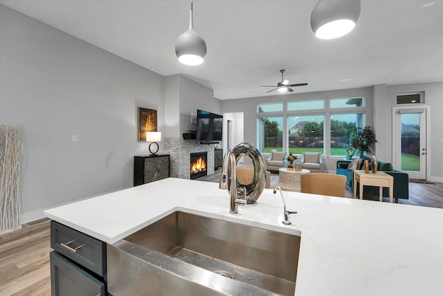 kitchen featuring a sink, light wood-type flooring, a lit fireplace, light countertops, and open floor plan