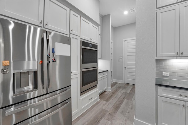 kitchen with light wood-style flooring, decorative backsplash, stainless steel appliances, baseboards, and visible vents