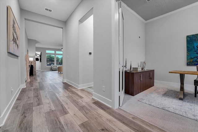 hall with baseboards, visible vents, wood finished floors, and crown molding