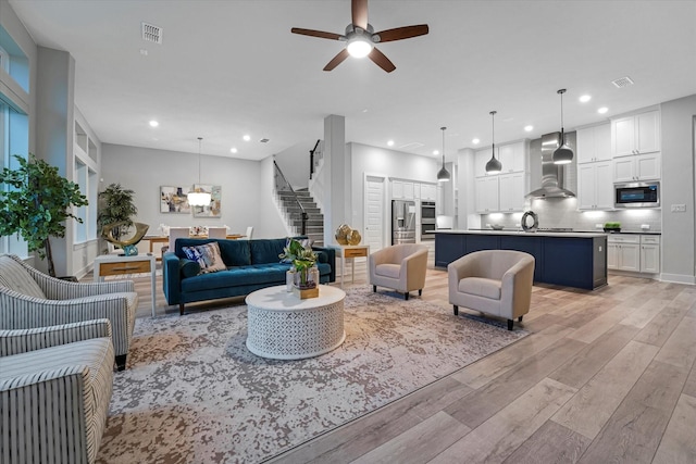 living area featuring visible vents, a ceiling fan, stairs, and light wood finished floors