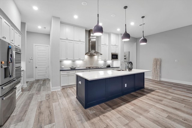 kitchen featuring light wood-style flooring, backsplash, wall chimney range hood, white cabinetry, and appliances with stainless steel finishes