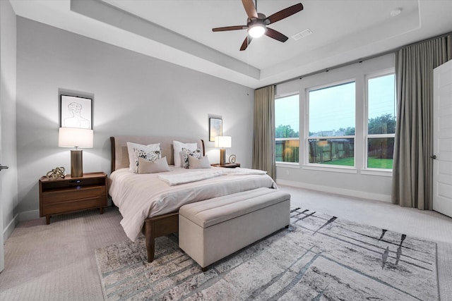 bedroom with carpet flooring, visible vents, ceiling fan, a tray ceiling, and baseboards