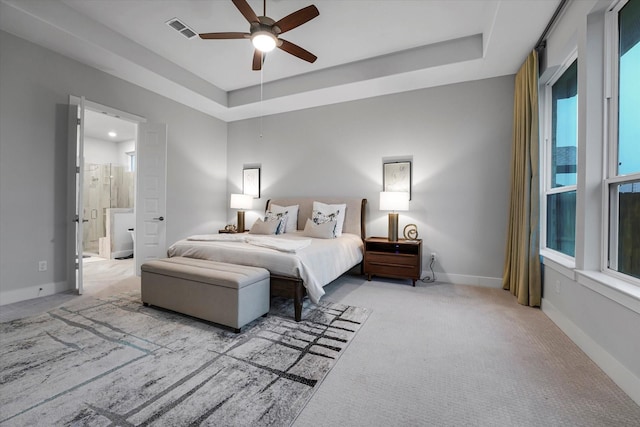 carpeted bedroom featuring ensuite bathroom, baseboards, visible vents, a raised ceiling, and a ceiling fan