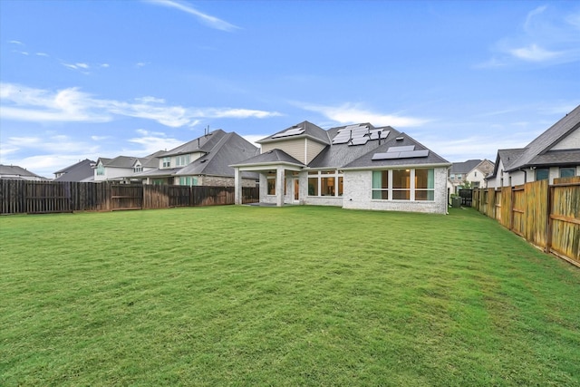 back of house featuring a fenced backyard, brick siding, a shingled roof, solar panels, and a lawn