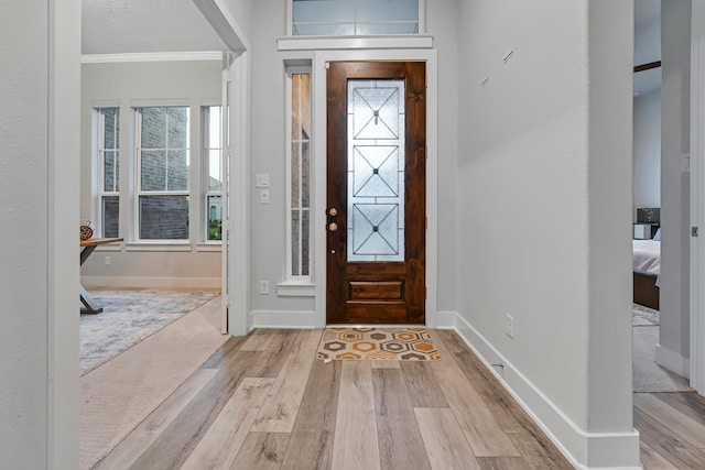 entrance foyer with ornamental molding, wood finished floors, and baseboards