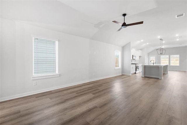 unfurnished living room with wood finished floors, baseboards, lofted ceiling, and visible vents