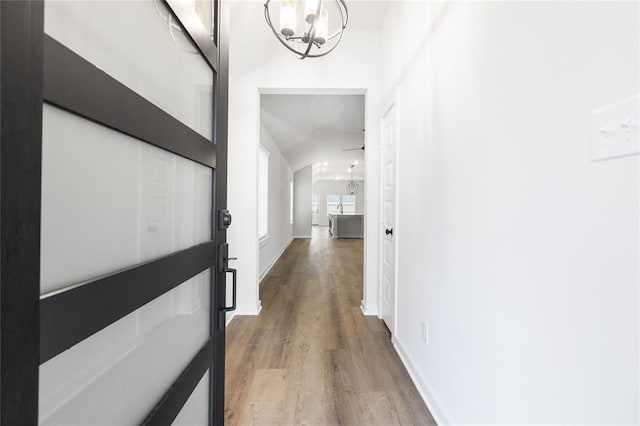 hallway featuring light wood finished floors, a notable chandelier, and baseboards