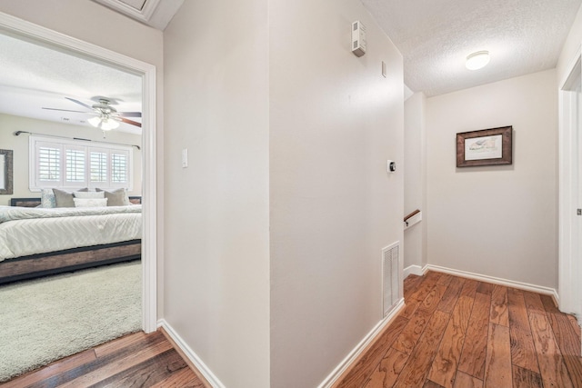 hall featuring visible vents, an upstairs landing, wood finished floors, and a textured ceiling