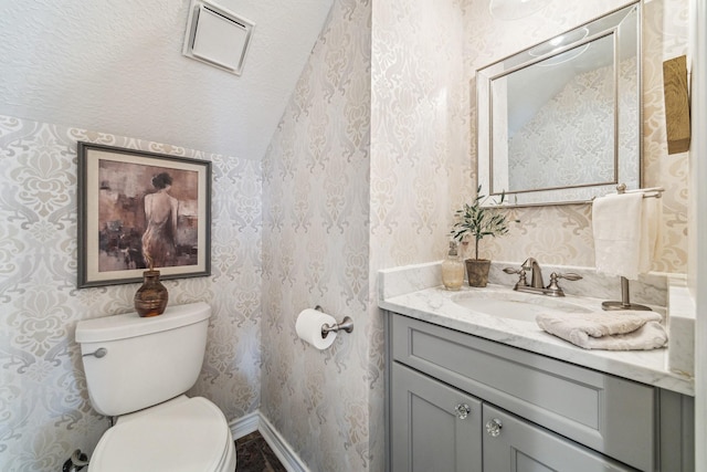 half bathroom featuring vanity, baseboards, wallpapered walls, toilet, and lofted ceiling