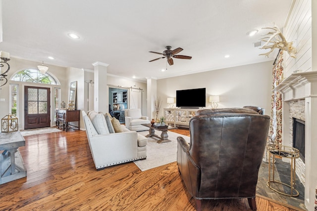 living area with ornamental molding, a fireplace, a ceiling fan, light wood-style floors, and decorative columns