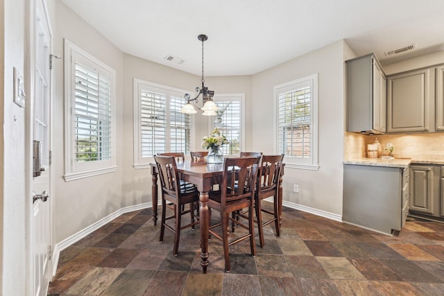 dining space featuring visible vents, baseboards, a chandelier, and stone tile flooring