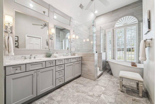 bathroom with ceiling fan, tiled shower, visible vents, a sink, and tile walls