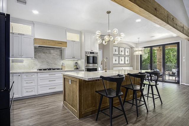 17939 Channel Hill Dr, Cypress, TX 77433 - kitchen with white cabinetry, appliances with stainless steel finishes, dark wood-style flooring, a center island with sink, and decorative backsplash