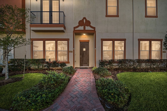 view of exterior entry featuring a yard and a balcony